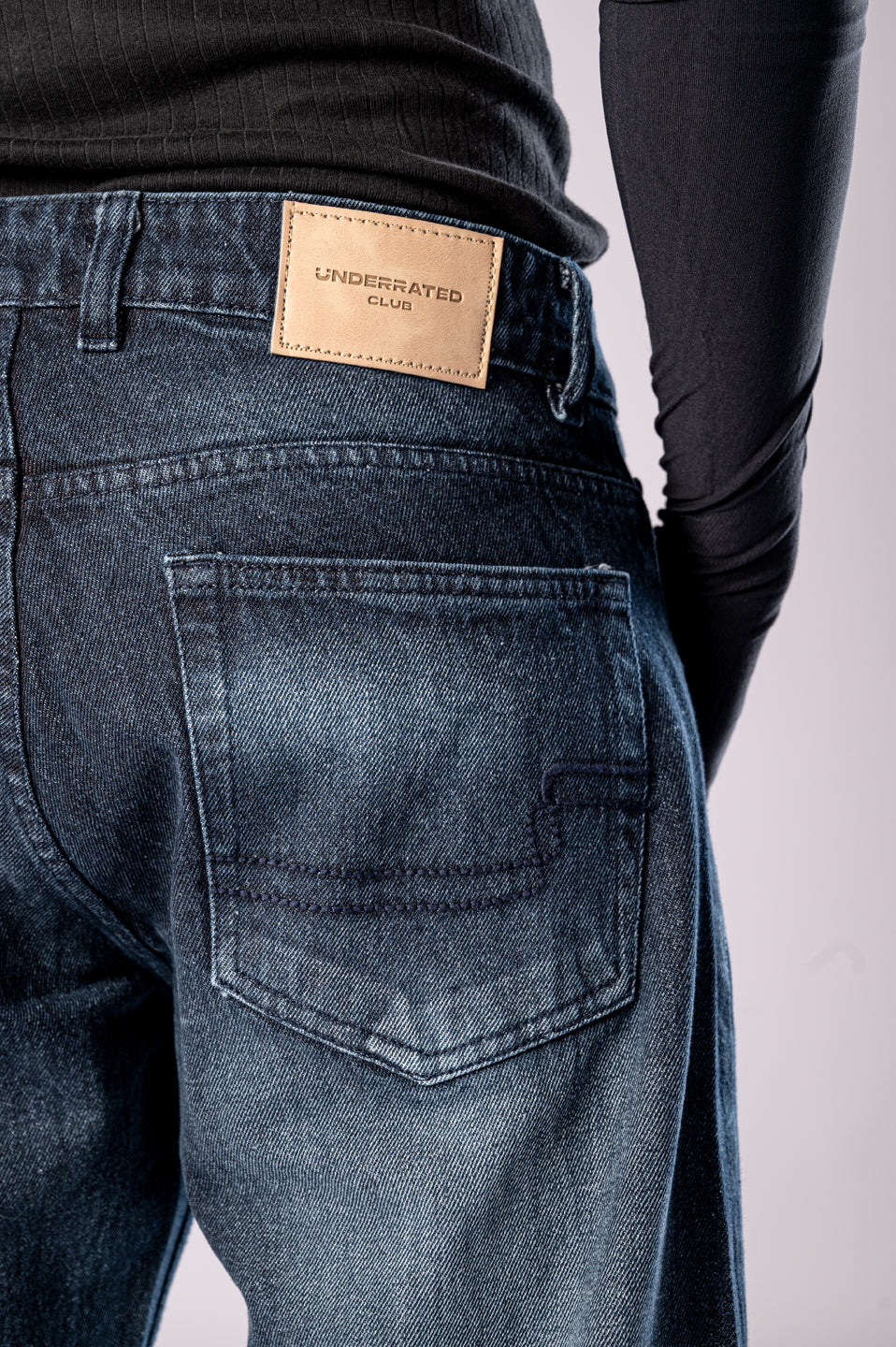 Close-up of the back of a person's dark-wash blue jeans, showing a tan leather patch on the waistband.
