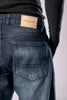 Close-up of the back of a person's dark-wash blue jeans, showing a tan leather patch on the waistband.