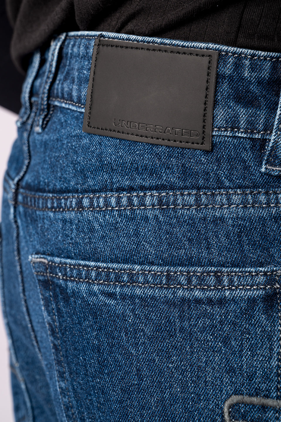 Close-up shot of the back of the dark blue jeans, focusing on the plain black leather patch on the waistband.