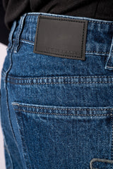 Close-up shot of the back of the dark blue jeans, focusing on the plain black leather patch on the waistband.