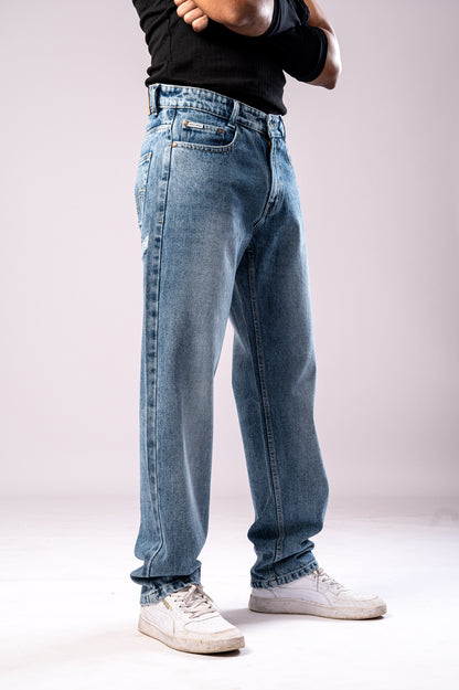 Angled side view of a person wearing light-wash blue baggy jeans, a black ribbed top, black arm sleeves, and white sneakers, with their arms crossed.