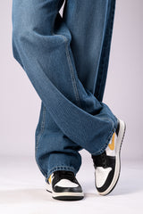 Close-up of a person's legs wearing light-wash blue baggy jeans, showing the wide fit and how they stack over black and white sneakers.