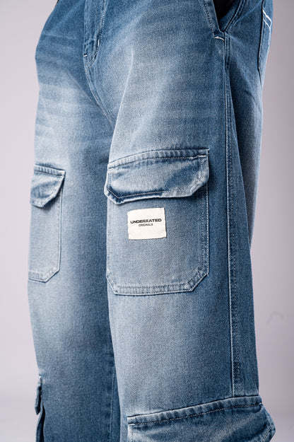 Close-up of the side cargo pocket on light-wash blue jeans, featuring a white Underrated Club logo patch.