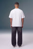 A man viewed from behind wearing a plain white short-sleeve t-shirt and dark charcoal gray baggy jeans, standing against a gray gradient studio background.