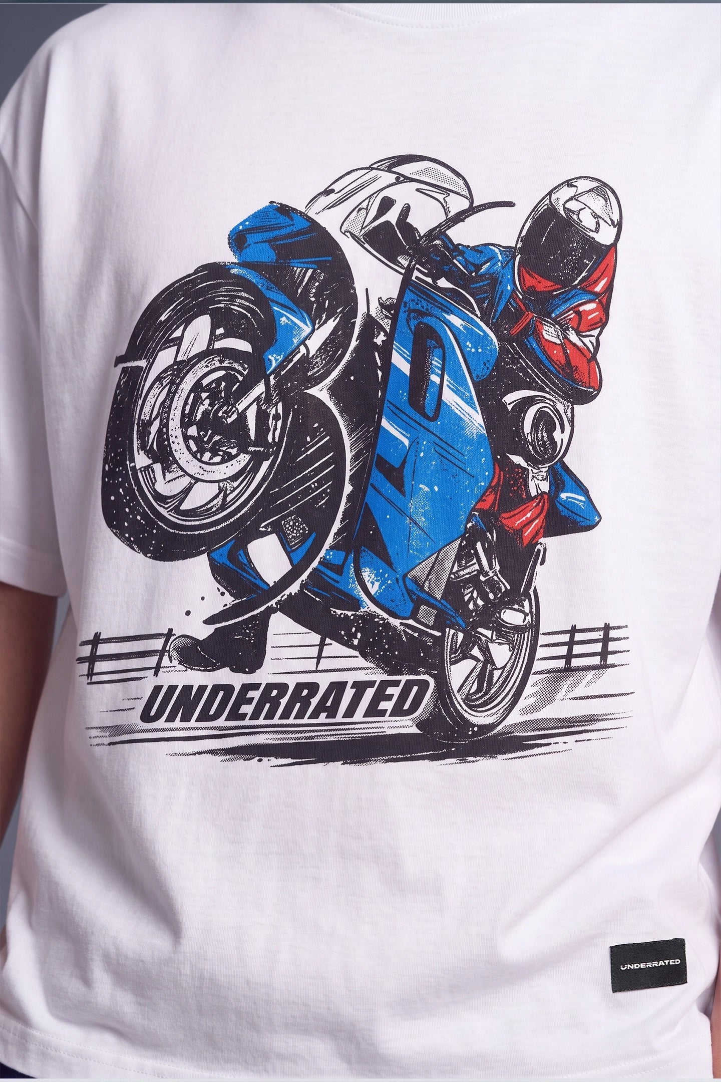 White short-sleeve graphic T-shirt featuring a large front print of a blue and red motorcycle with a rider and the word 'UNDERRATED' below it.