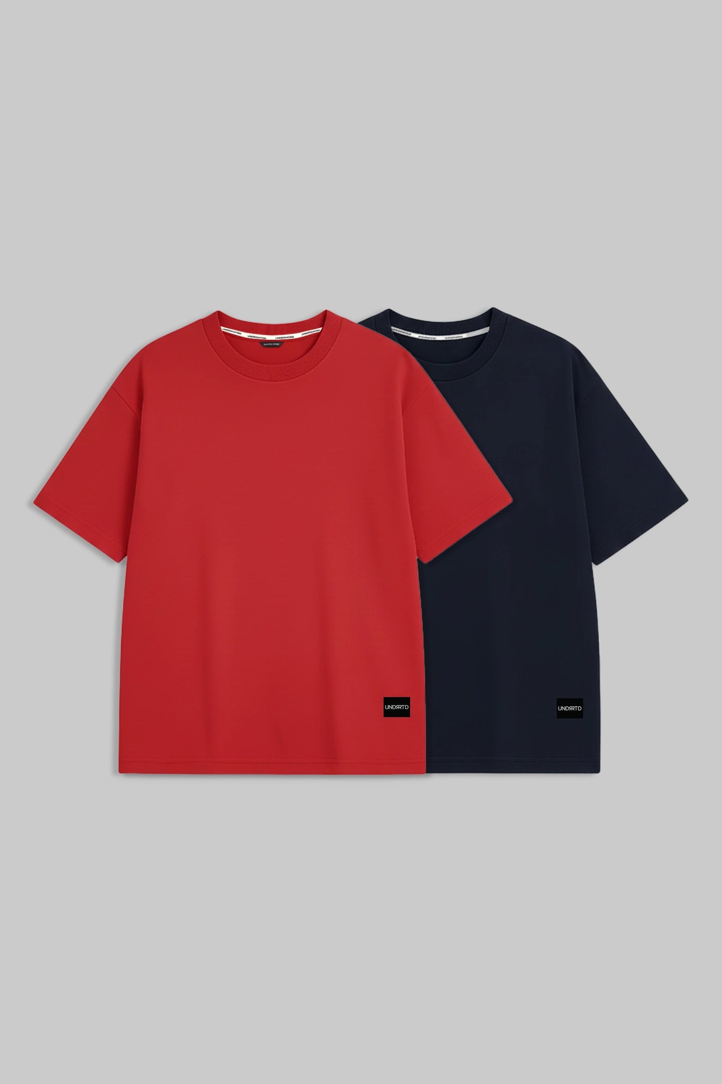 Two short-sleeve crewneck t-shirts displayed side by side on a solid gray background. The front t-shirt is a vibrant red, and the t-shirt behind it is navy blue.