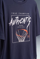 A navy blue oversized t-shirt featuring a basketball-themed graphic print with the text 'TRUE CHAMPION Authentic BORN ORIGINAL' and an orange basketball hoop illustration.