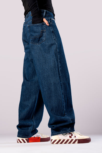 Angled side view of a person wearing baggy, dark blue jeans, showing the loose fit of the pants.