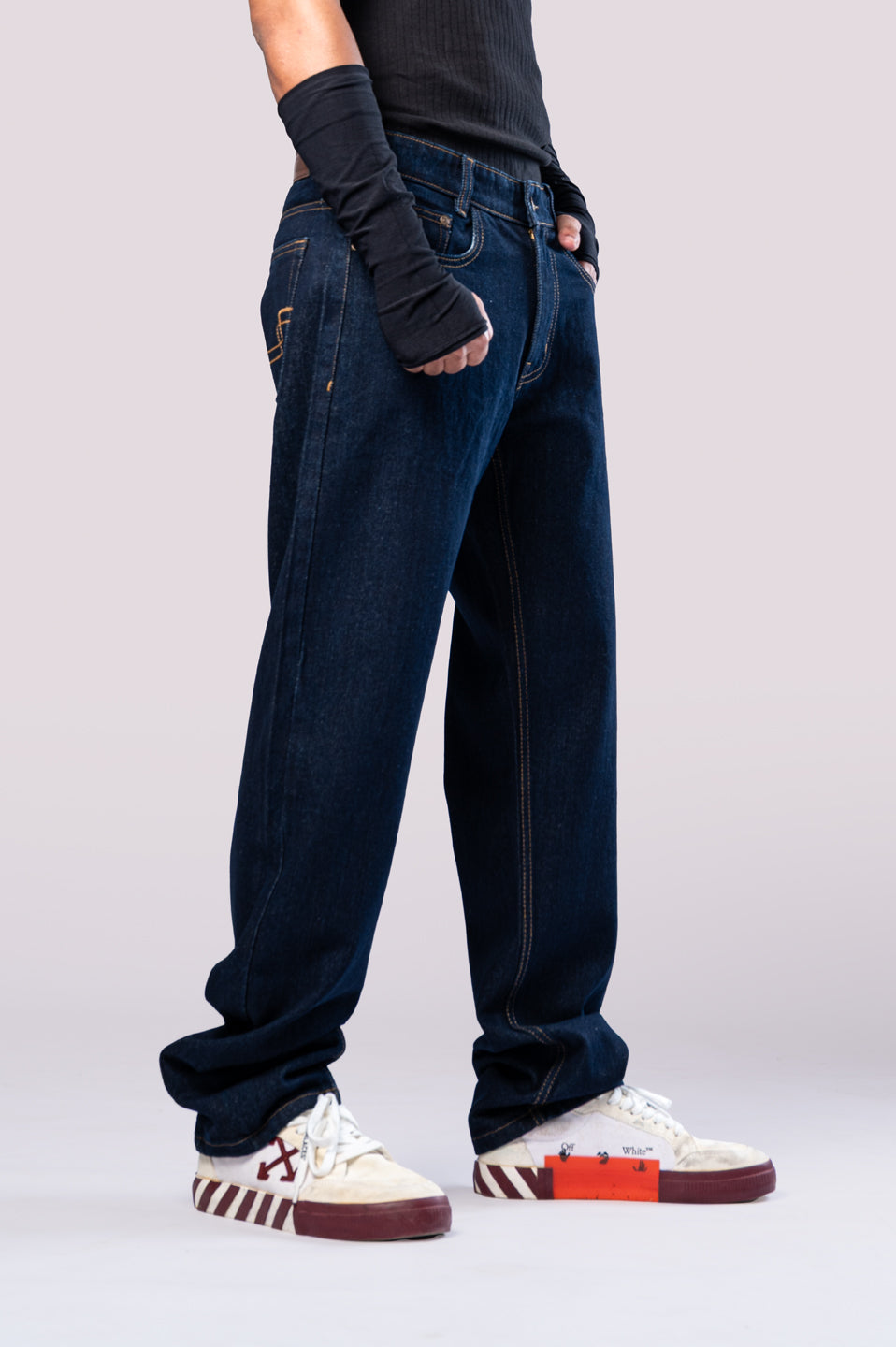 Angled side view of a person wearing dark-wash blue baggy jeans, showing the loose fit and stacking at the ankles.
