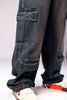 Close-up side view of the leg of a person wearing dark, rusty-blue baggy cargo jeans, showing the detail and texture of the stacked cargo pockets.