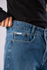 Close-up of the front pocket of dark-wash blue jeans, showing a small white 