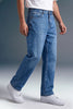 A person wearing light-to-medium blue denim jeans with a white t-shirt and white sneakers, shown from the waist down against a studio background.