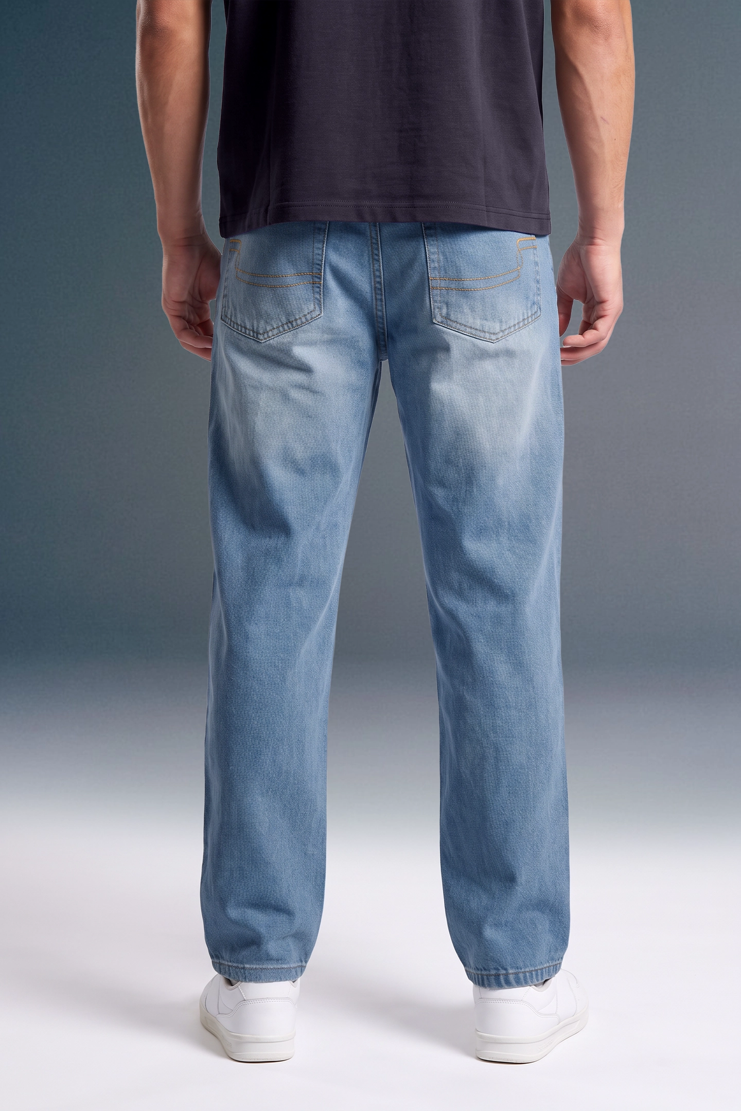 A person shown from the back wearing light-wash blue jeans, a dark navy T-shirt, and white sneakers against a studio background.