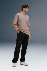 A man wearing a taupe t-shirt and black cargo pants with white contrast stitching and white sneakers.