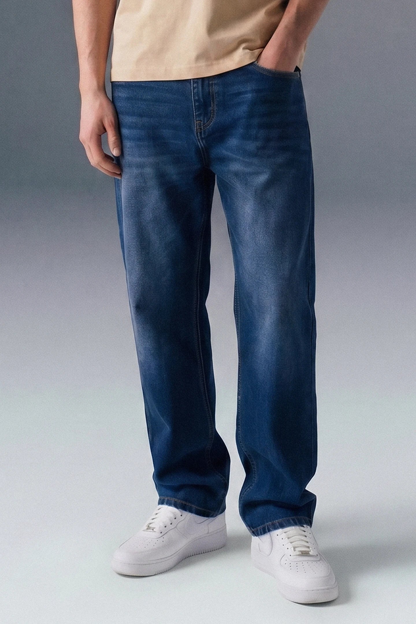 Person wearing blue jeans and white sneakers on a gray background