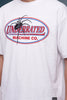 A white short-sleeve t-shirt featuring a large graphic on the chest of a black spider over an oval logo that reads 'UNDERRATED MACHINE CO.' in red and blue text.