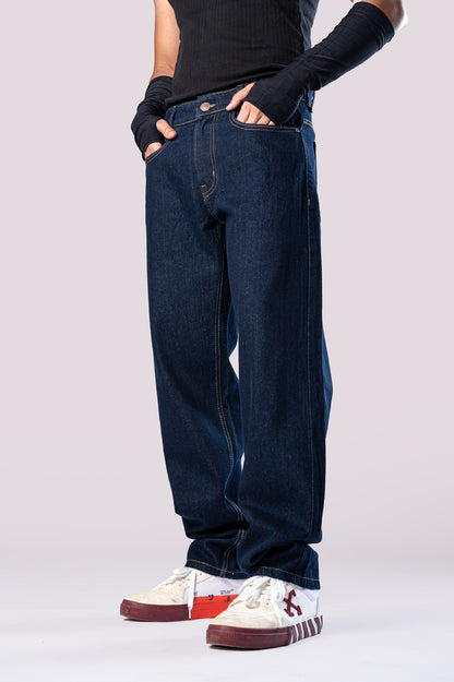 Side view of a person wearing dark-wash blue baggy jeans, a black ribbed top, black arm sleeves, and white and maroon sneakers, with their hands in their pockets.