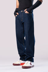 Side view of a person wearing dark-wash blue baggy jeans, a black ribbed top, black arm sleeves, and white and maroon sneakers, with their hands in their pockets.