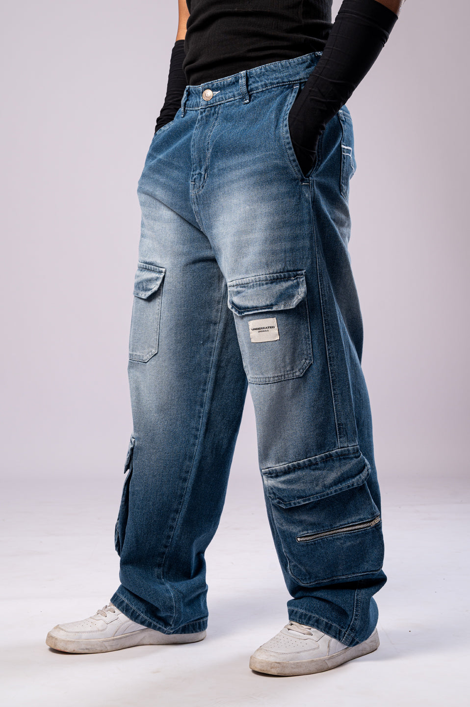 Angled side view of a person wearing light-wash blue baggy cargo jeans, showing the multiple pockets and loose fit.