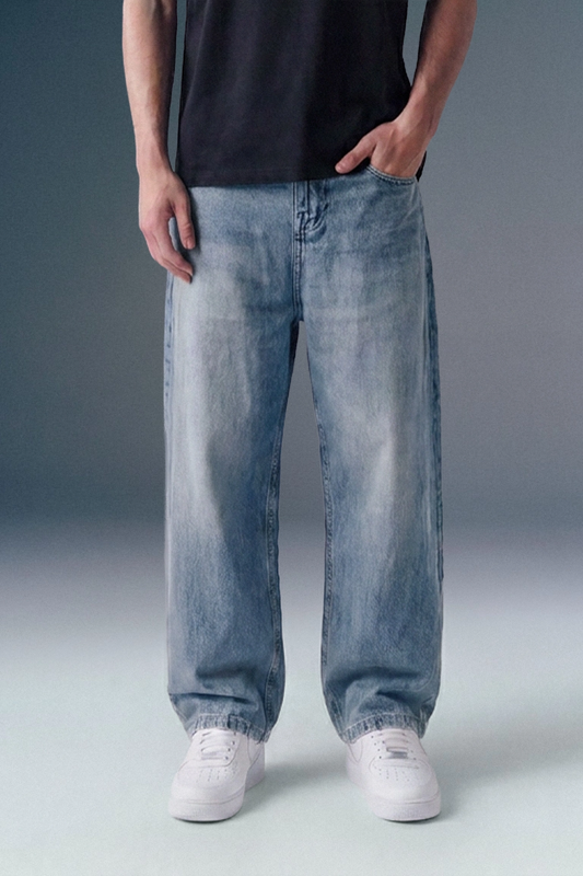 Front view from the waist down of a man standing with one hand in his pocket, showcasing a pair of straight-leg, light-wash blue denim jeans with subtle fading along the front of the legs, paired with white shoes.