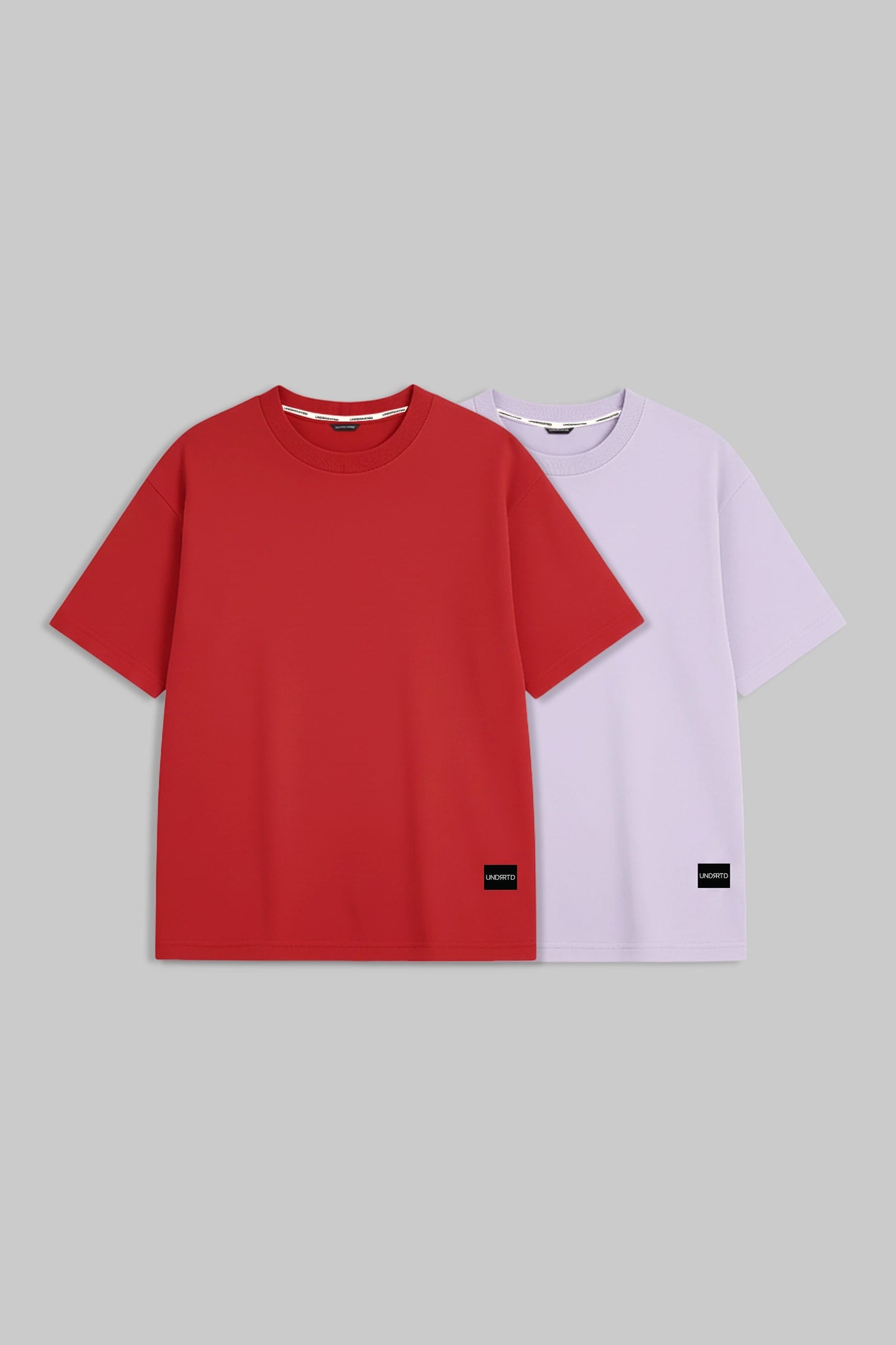 Two short-sleeve crewneck t-shirts displayed side-by-side on a solid gray background. The front t-shirt is a vibrant red, and the t-shirt behind it is a pale lavender purple.