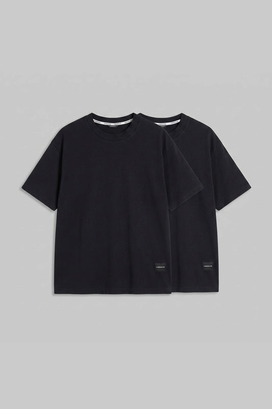 Two black short-sleeve crewneck t-shirts displayed in a layered flat-lay arrangement on a solid gray background.