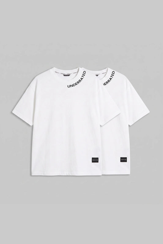 Two white short-sleeve T-shirts by Understood, arranged overlapping on a light gray background. The front shirt has black text reading 'UNDERSTOOD' across the chest and a small black label near the hem, while the rear shirt shows 'UNDERSTOOD' on the shoulder strap.