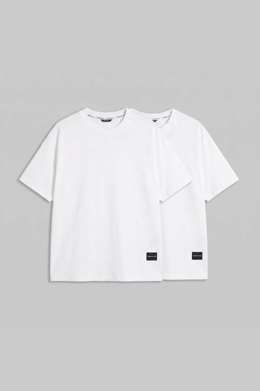 Two white short-sleeve crewneck t-shirts with small black rectangular labels near the lower hem, displayed against a solid gray background.