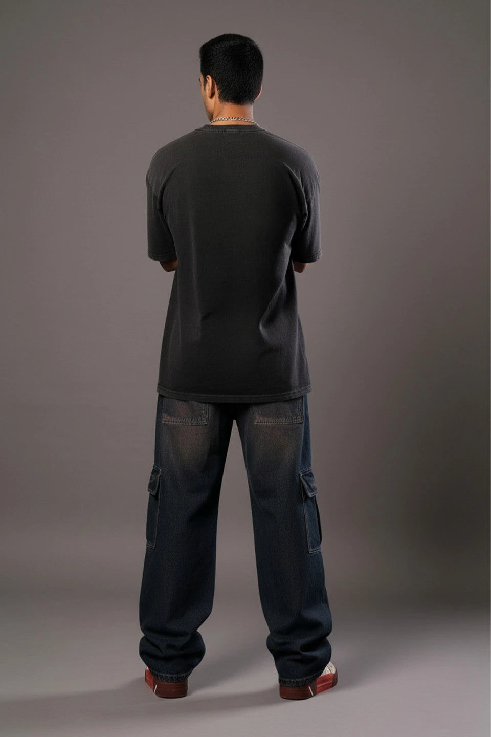 Rear view of a man in a dark grey t-shirt and baggy dark blue cargo jeans with large side pockets.