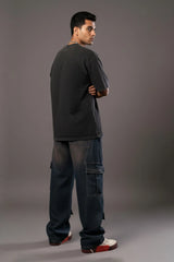 Side view of a man in a black tee and baggy cargo jeans with large utility pockets on the leg.