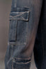 Close-up of a large utility cargo pocket on the side of dark blue denim jeans with decorative stitching.