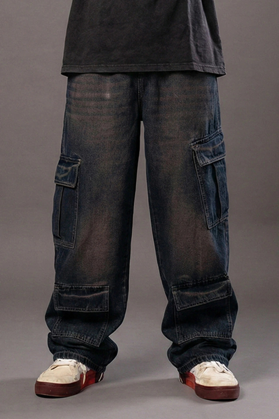 Rear view of a man in a dark grey t-shirt and baggy dark blue cargo jeans with large utility pockets.
