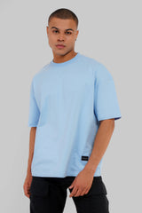 A man wearing a light blue oversized crewneck t-shirt and black cargo pants, standing against a solid gray studio background.