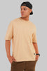 A man wearing a light beige crew-neck t-shirt, brown pants, and a black baseball cap, photographed against a solid gray background.