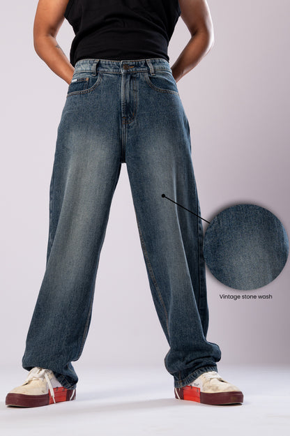 Model in dark wash baggy jeans with a skateboard, showing the full length.