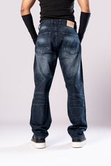 Full-body front view of a person wearing dark-wash blue baggy jeans with ripped knees, a black top, and black arm sleeves, with their hands in their pockets.