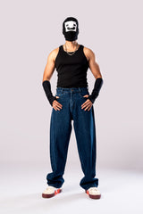 Full-body front view of a person wearing baggy, dark blue jeans with a black tank top, black arm sleeves, and a white cap.