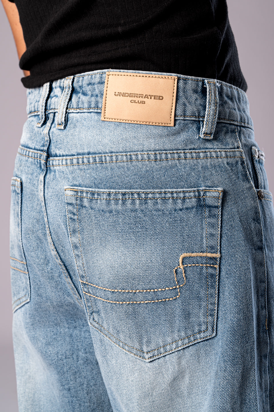 Close-up of the back of the light wash jeans, showing the leather brand patch and pocket detail.