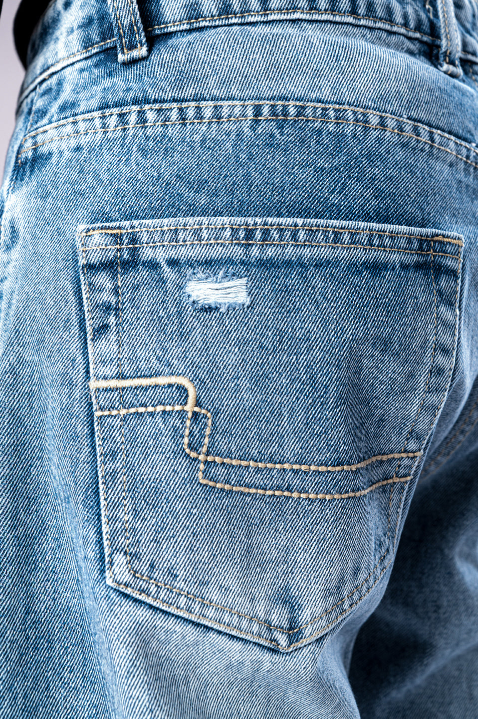Close-up of the back pocket of light-wash blue jeans, showing detailed stitching and a small distressed rip.