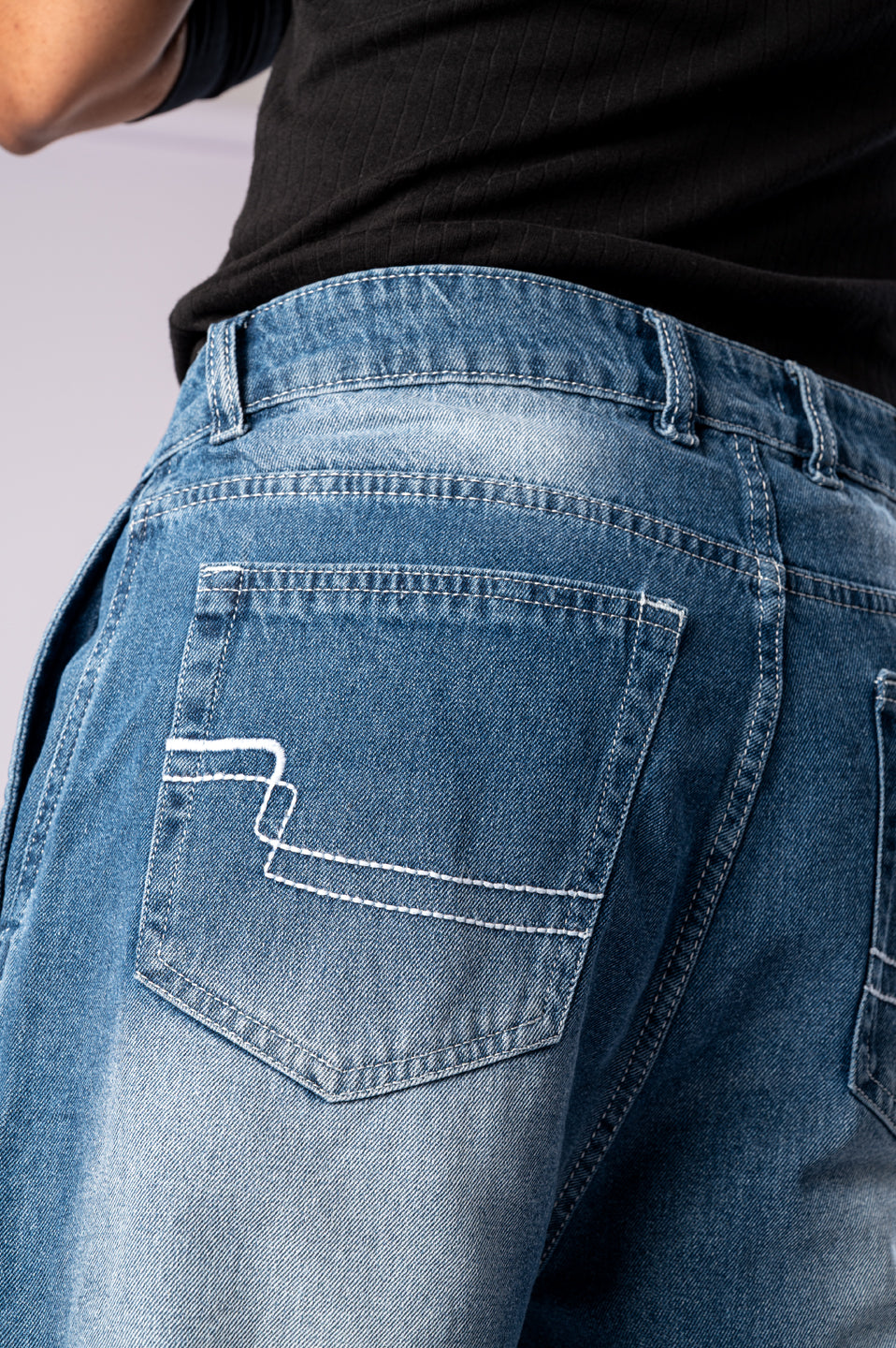 Close-up of the back pocket of light-wash blue jeans, showing white decorative stitching.