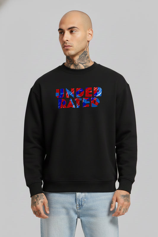 Man wearing a black “Underrated Originals” crewneck sweatshirt layered over a white collared shirt, paired with light blue jeans, standing against a plain grey background.