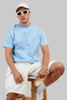 Light blue t-shirt model sunglasses seated white sneakers jeans summer streetwear Underrated Club.
