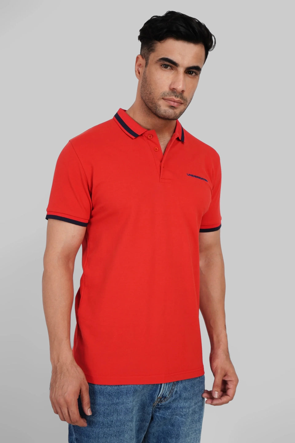 A man in a bright red polo shirt with black and yellow collar detailing standing against a grey background.