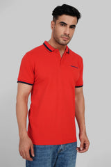 A man in a bright red polo shirt with black and yellow collar detailing standing against a grey background.
