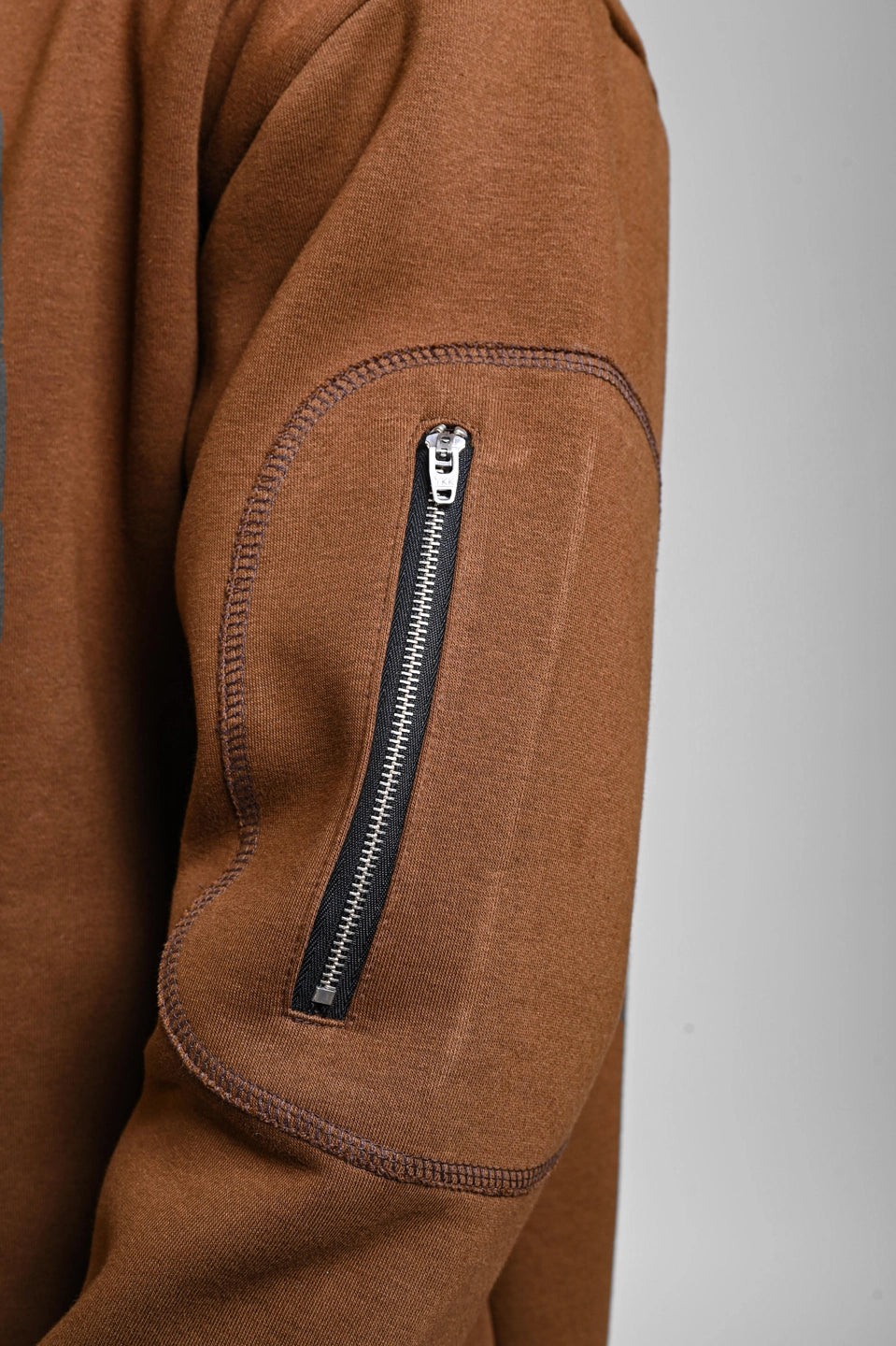 Close-up of brown men’s sweatshirt sleeve featuring zippered utility pocket and reinforced elbow patch.