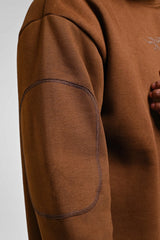 Close-up of brown men’s sweatshirt sleeve showing reinforced elbow patch and premium fabric texture.