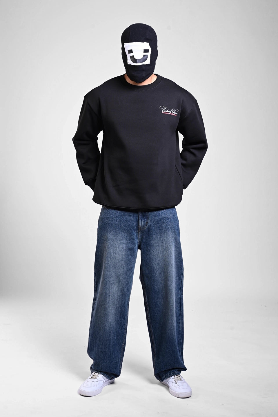 Full-body view of a person in a black "Evolving Vision" sweatshirt, baggy blue jeans, and white sneakers.