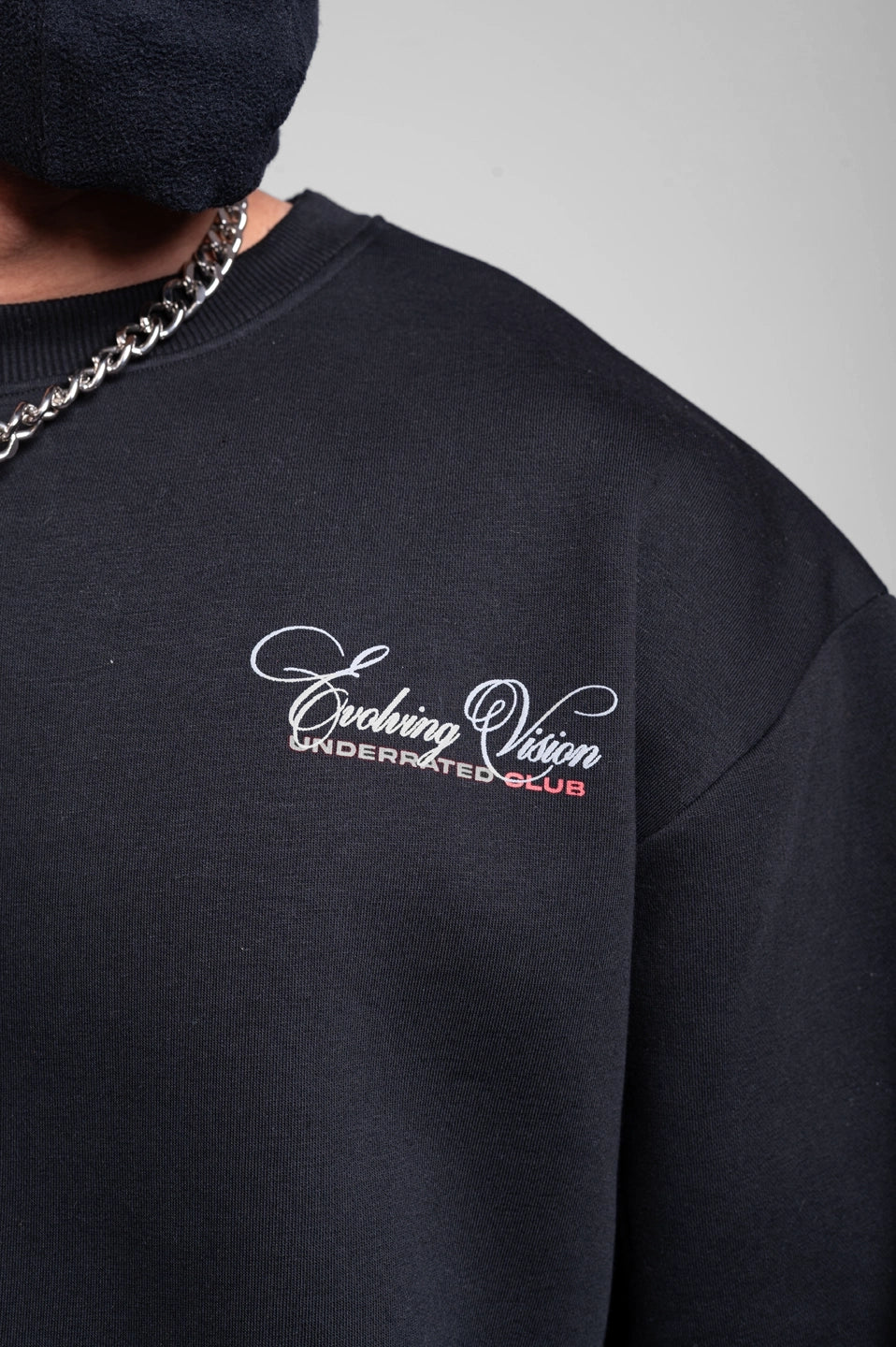 Close-up of black men’s sweatshirt featuring embroidered “Evolving Vision” logo and ribbed crew neck.