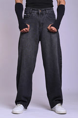 Front view of a person wearing oversized, dark grey acid-wash jeans and white sneakers against a plain background.