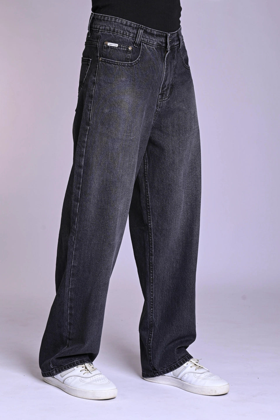 Front view of a person wearing oversized, dark grey acid-wash jeans and white sneakers against a plain background.